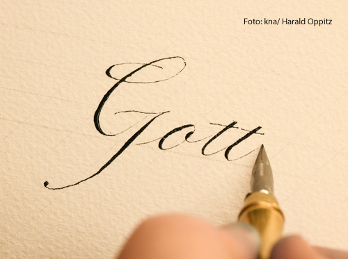 Jemand schreibt das Wort "Gott" mit einer Feder auf ein Blatt Papier.