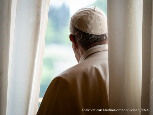 Papst Franziskus steht hinter einem Vorhang und guckt aus einem Fenster im Apostolischen Palast am 20. Mai 2020 im Vatikan.