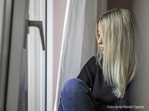 Eine Frau blickt traurig aus dem Fenster. 