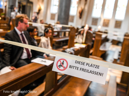 Auf einem Schild an einer Kirchenbank steht der Hinweis "Diese Plätze bitte freilassen."