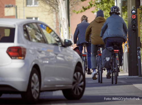 Radfahrer ueberqueren eine Strasse in Berlin, bevor ein Auto Rechts abbiegt.