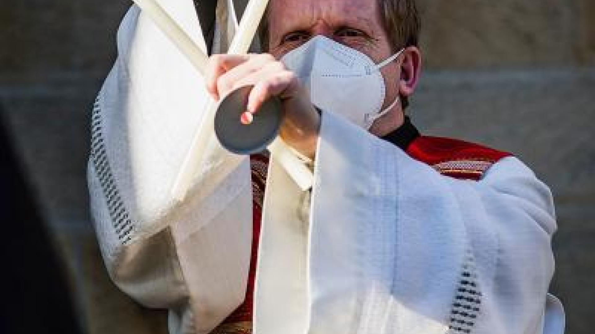 Priester spendet den Blasiussegen mit zwei gekreuzten Kerzen in der Hand