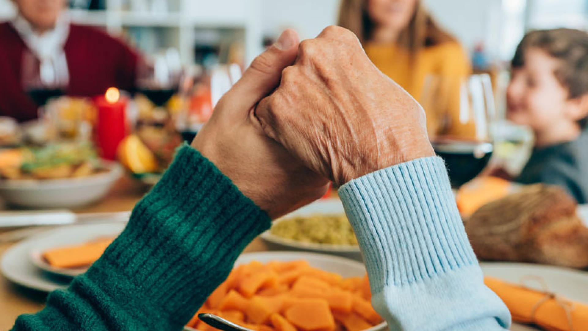 Familie am Tisch fasst sich an den Händen beim Gebet.