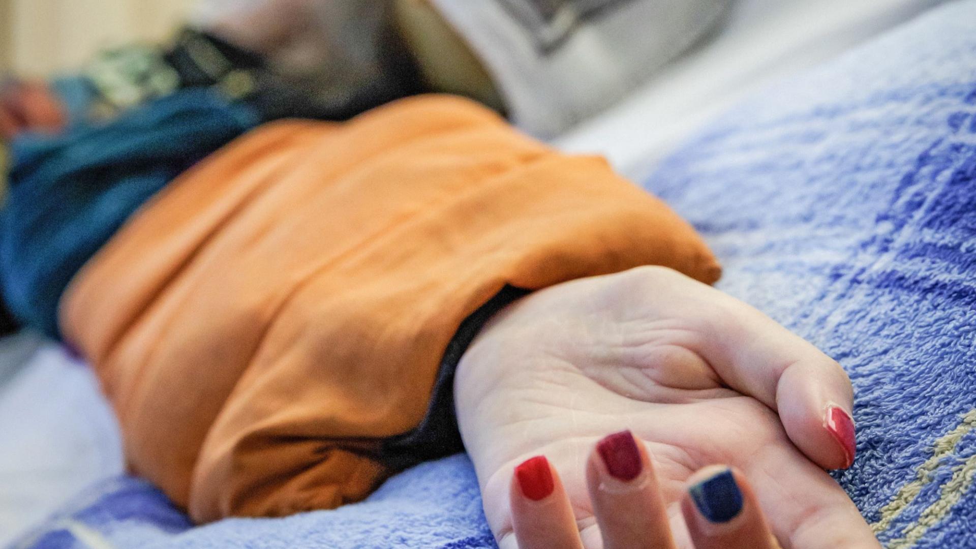 Eine Hand mit bunt lackierten Fingernägeln, die auf einem Bett liegt