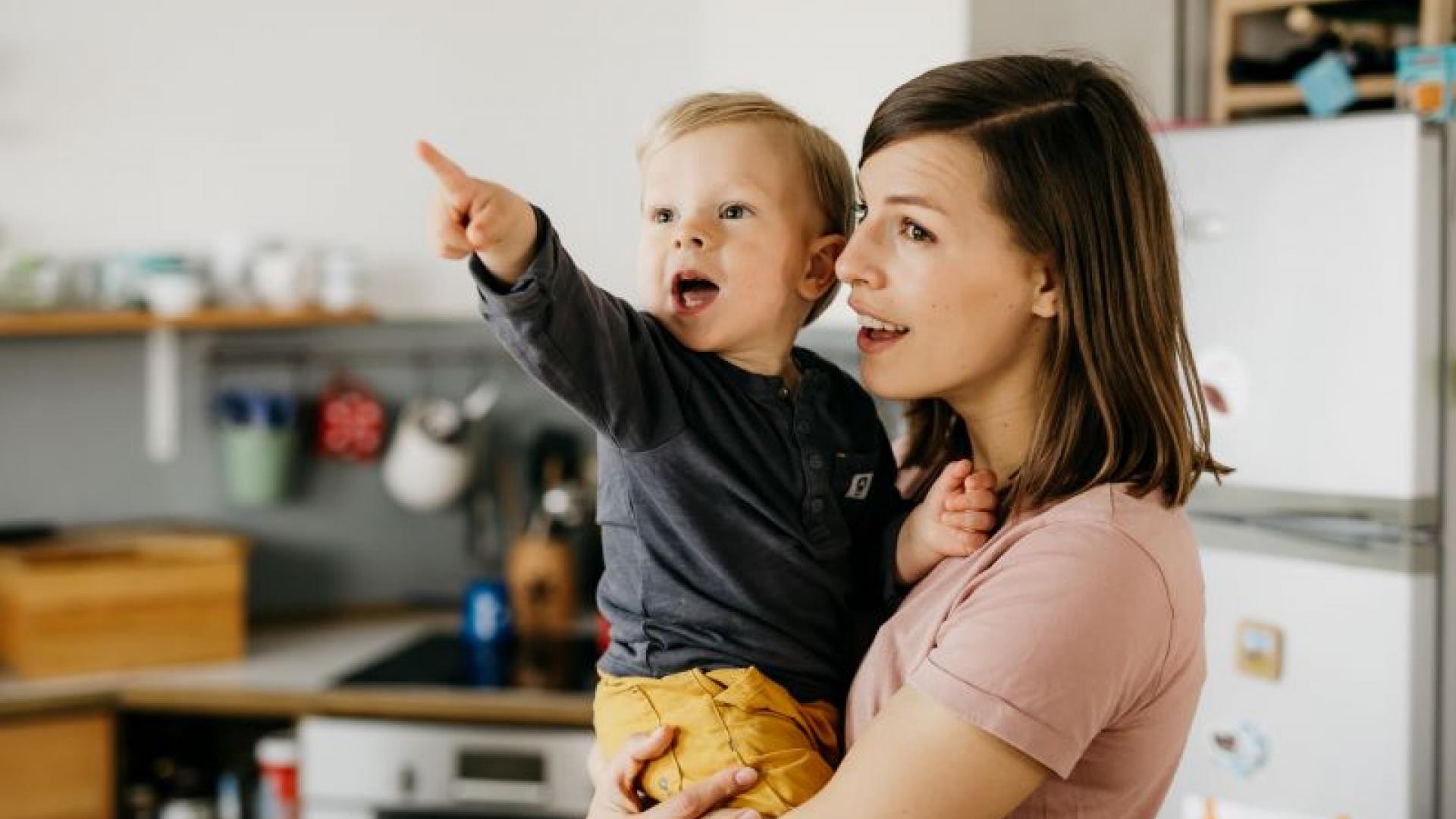 Mutter trägt ihr Kind auf dem Arm, das mit dem Finger auf etwas zeigt
