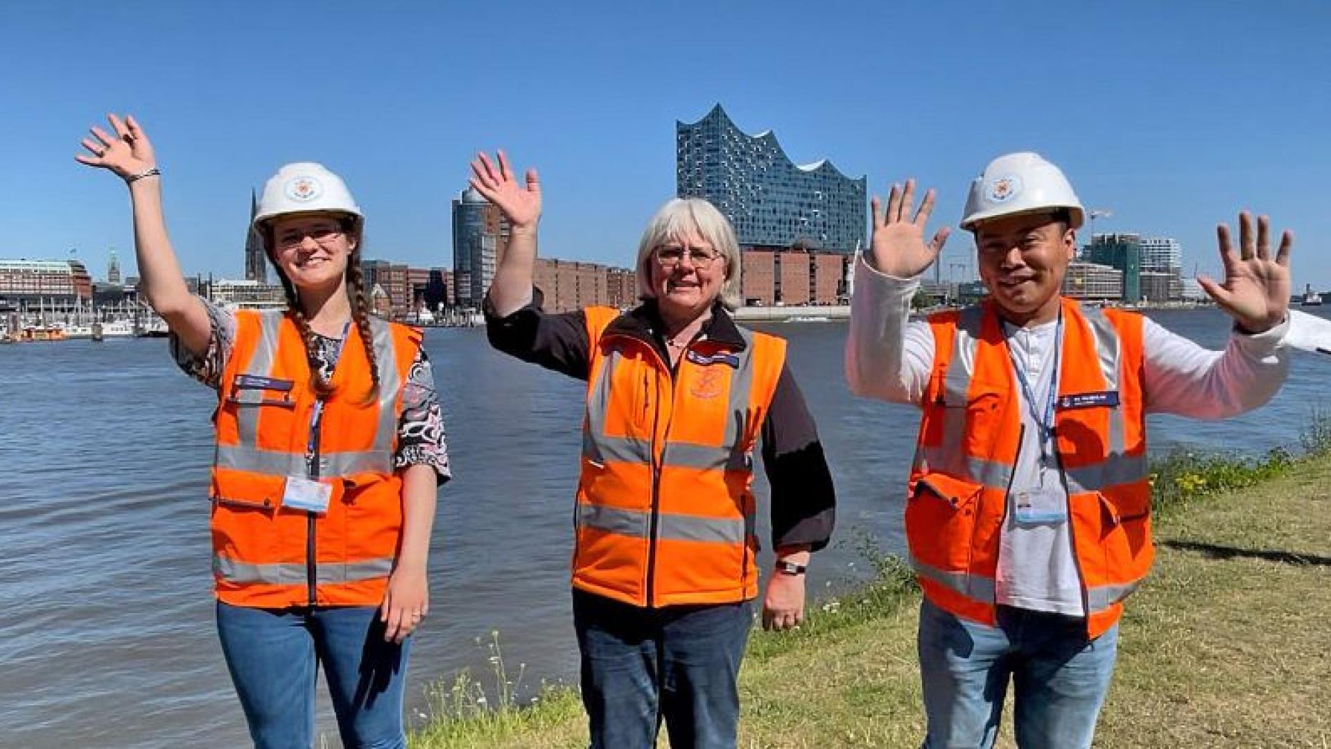 Drei Seelsorger winken vor der Elbe und der Elbphilharmonie in Hamburg