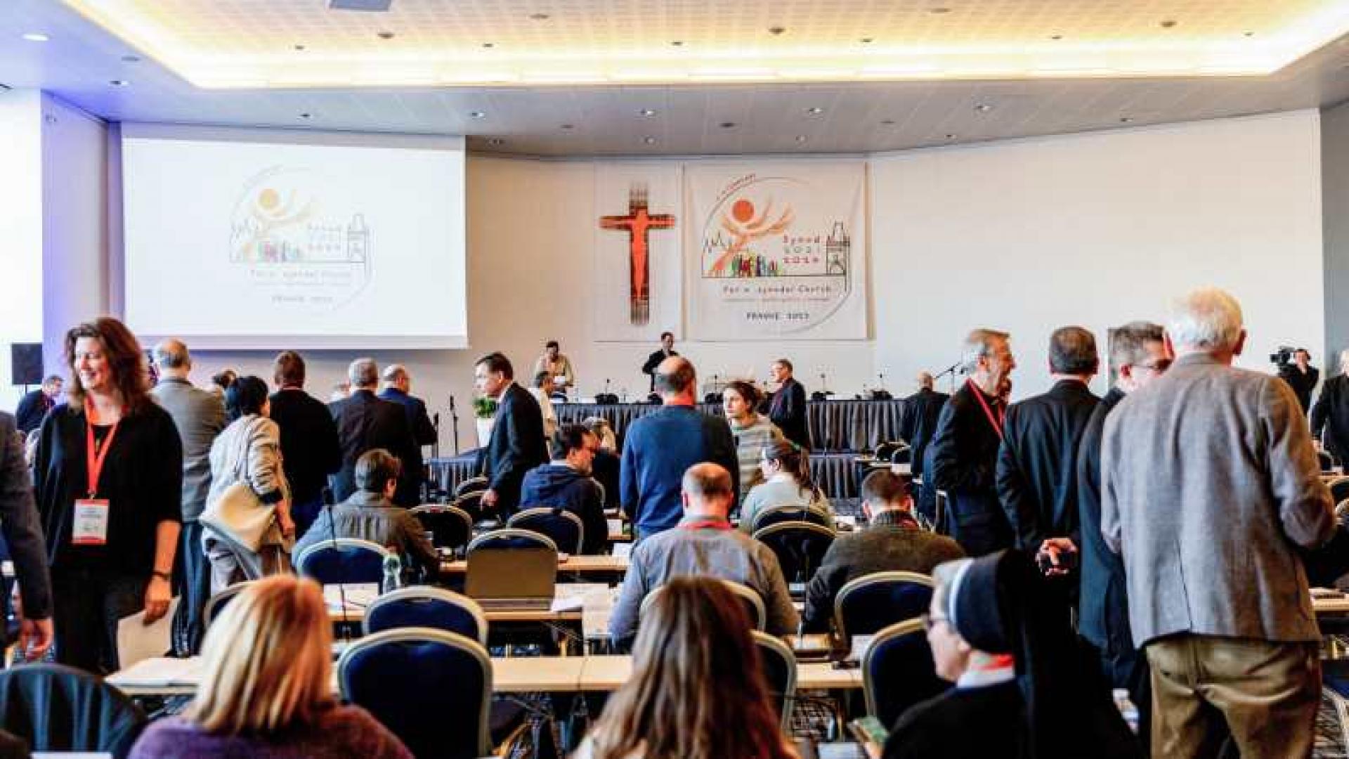 Teilnehmer unterhalten sich im Sitzungssaal der Europa-Etappe der Weltsynode am 7. Februar 2023 in Prag (Tschechien). An der Wand im Hintergrund hängt das Logo der Weltsynode.
