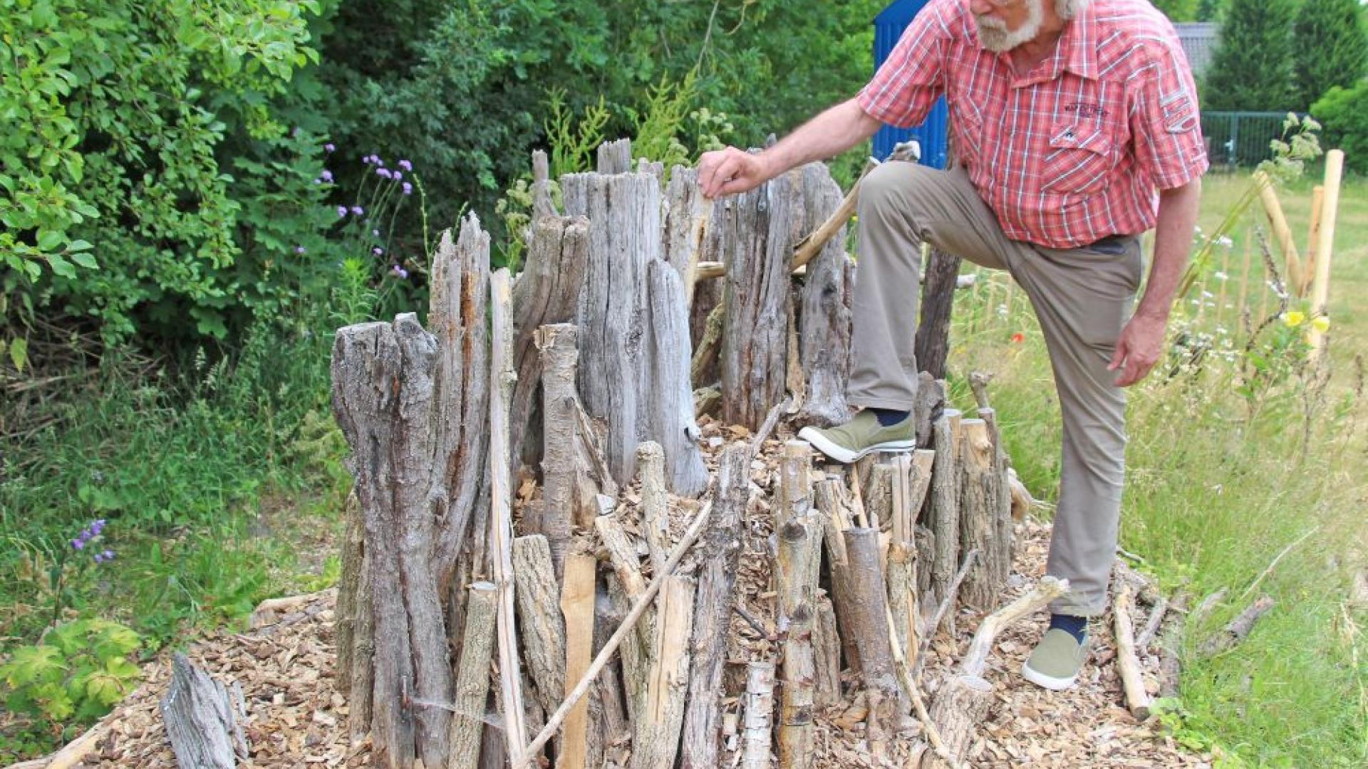 Mann im Garten vor einem Haufen Totholz