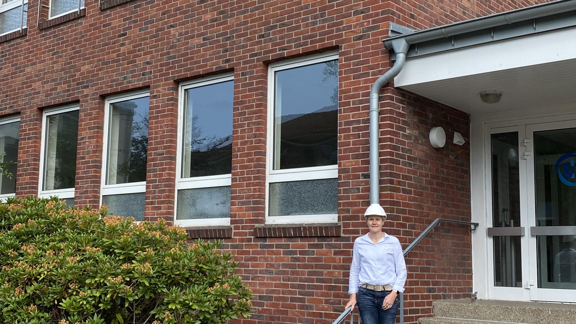 Eine Frau steht auf einer Treppe vor einer Schule.