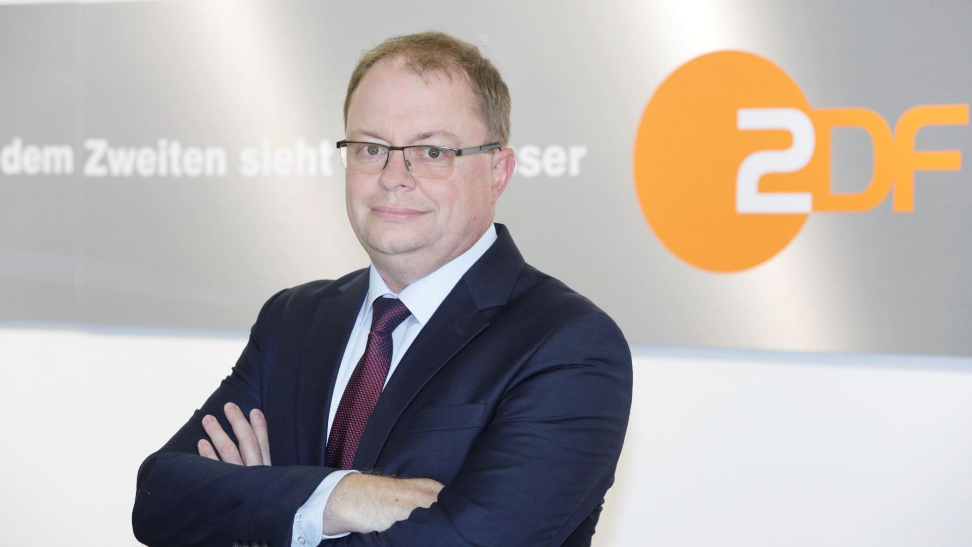 Redaktionsleiter Jürgen Erbacher vor dem Logo des ZDF