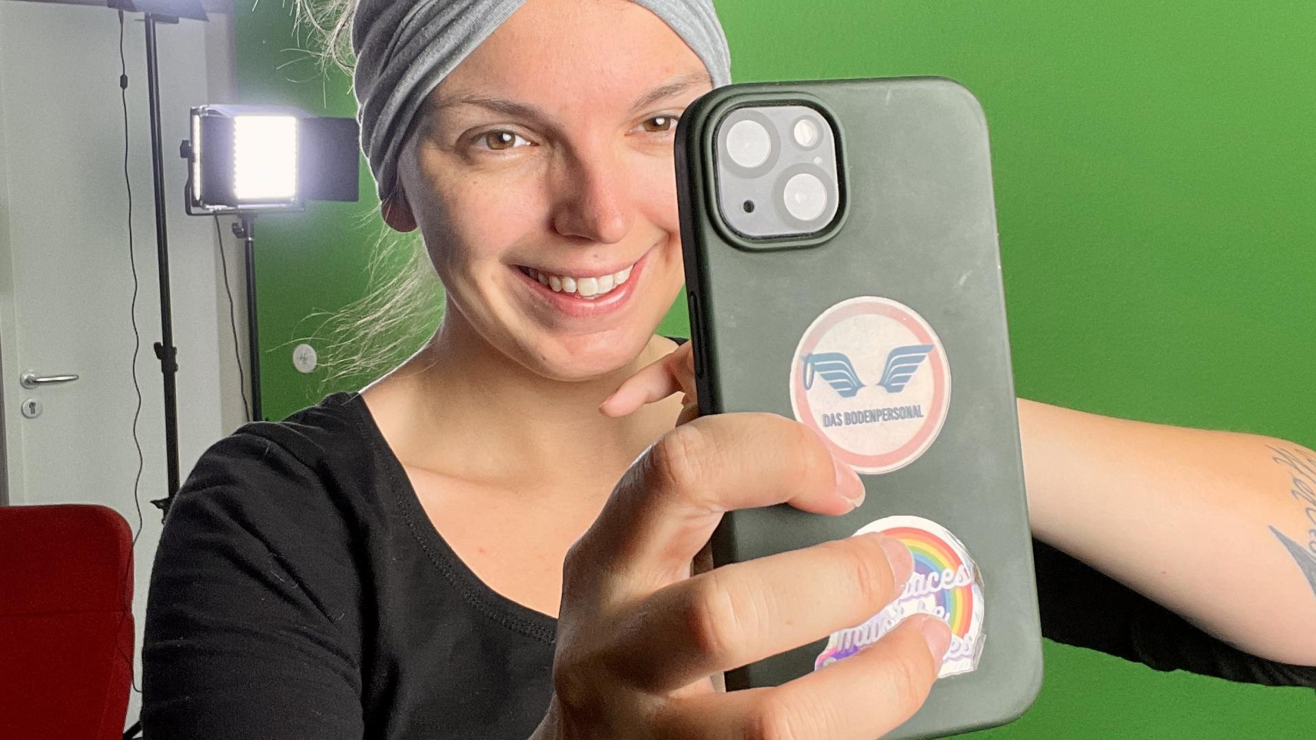 Eine Frau mit einem Handy vor einer grünen Wand.