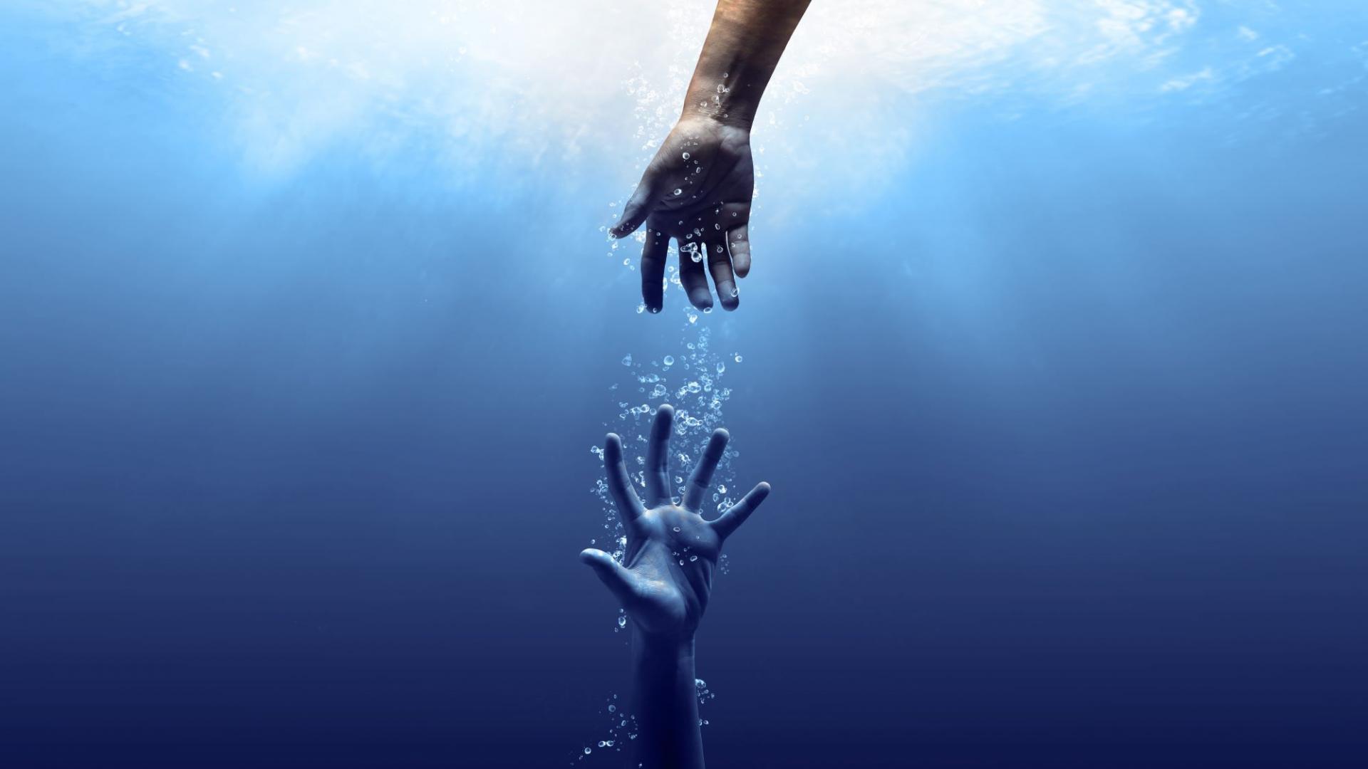 Eine Hand greift unter Wasser nach einer anderen Hand, die droht zu versinken
