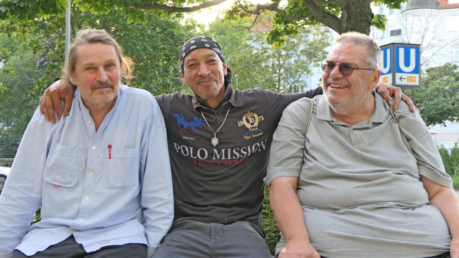 Drei Menschen halten einander im Arm und sitzen gemeinsam auf einer Bank