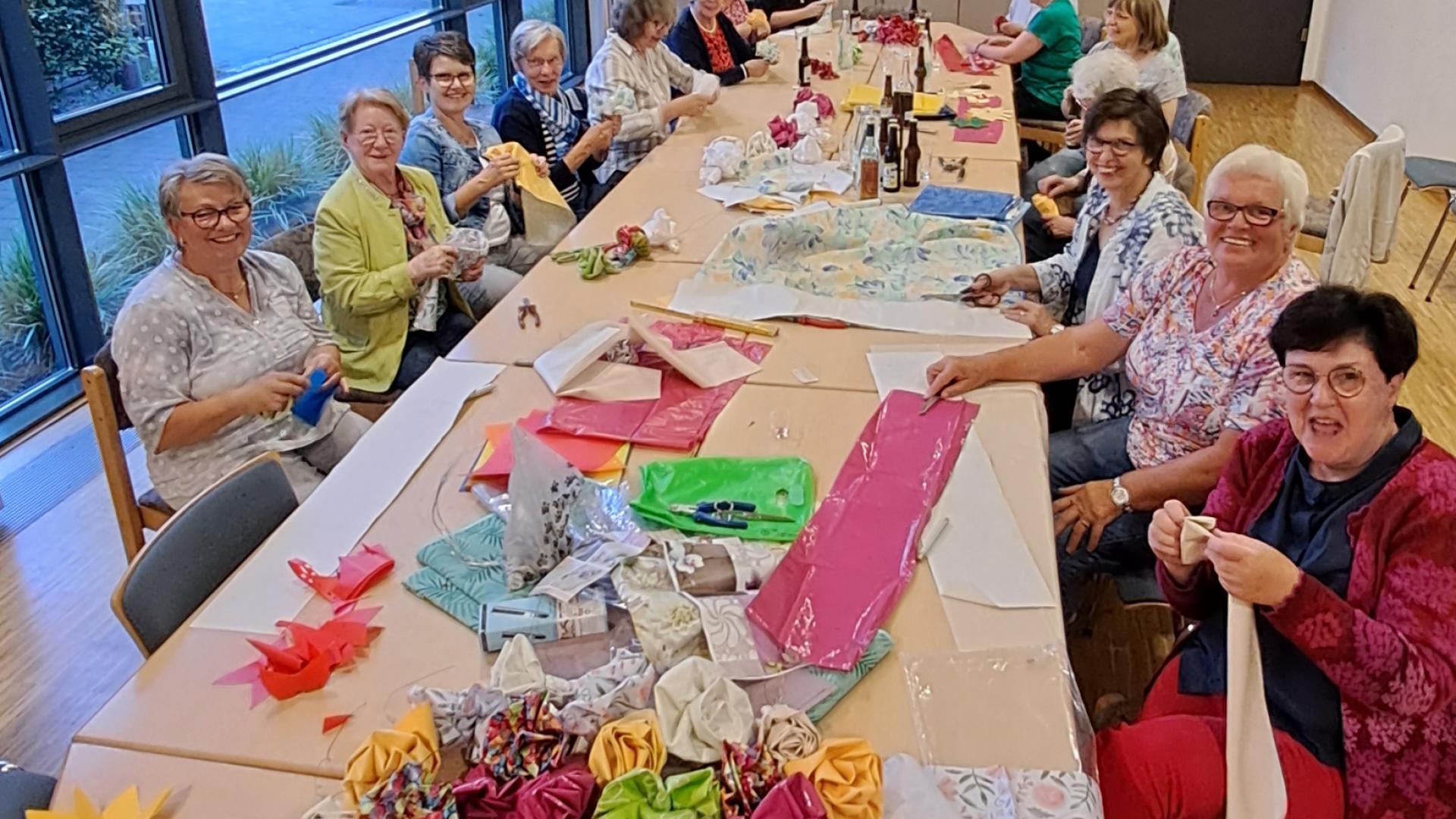 Frauen sitzen am Tisch und basteln Blumen.
