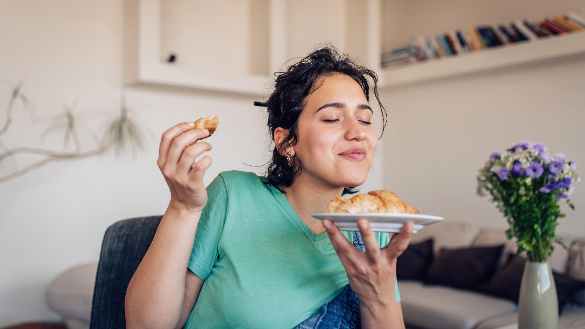 Junge Frau isst sichtlich mit Genuss einen Croissant.