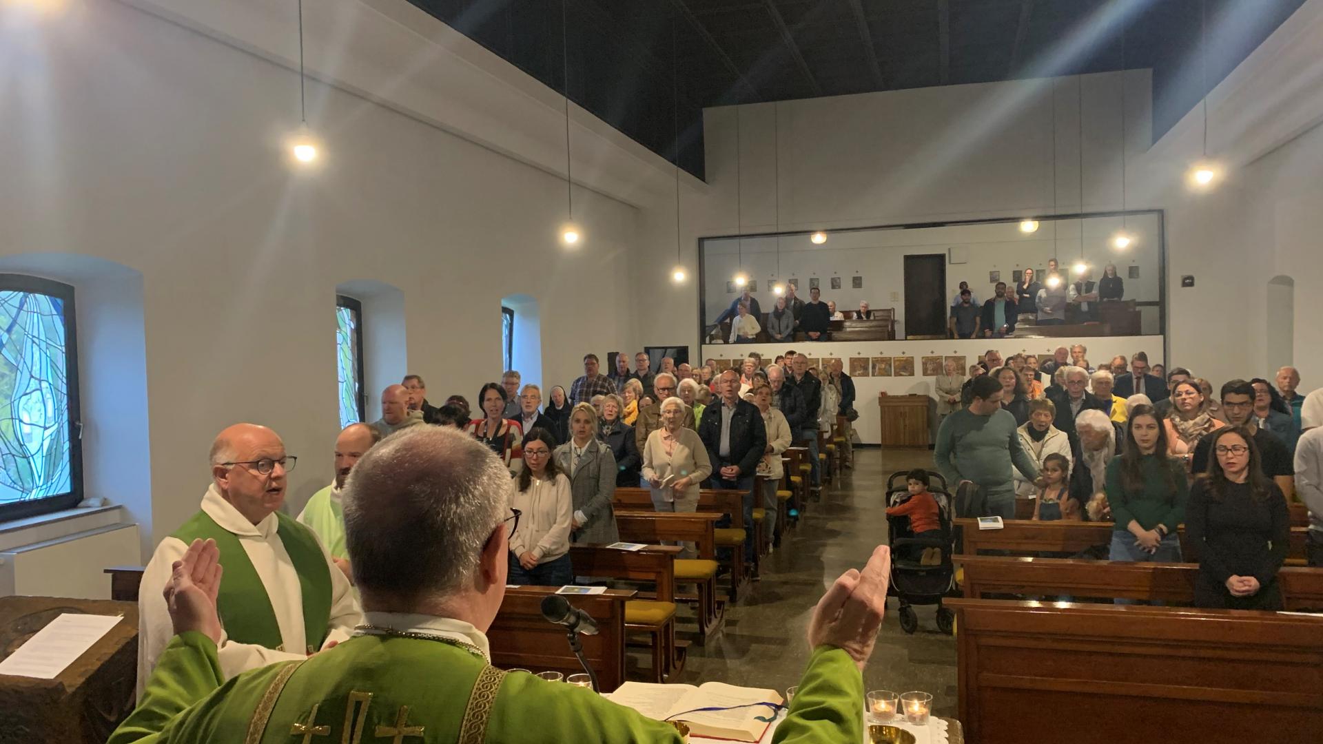 Ein Priester steht hinter dem Altar, mehrere Gläubige stehen in den Bänken.