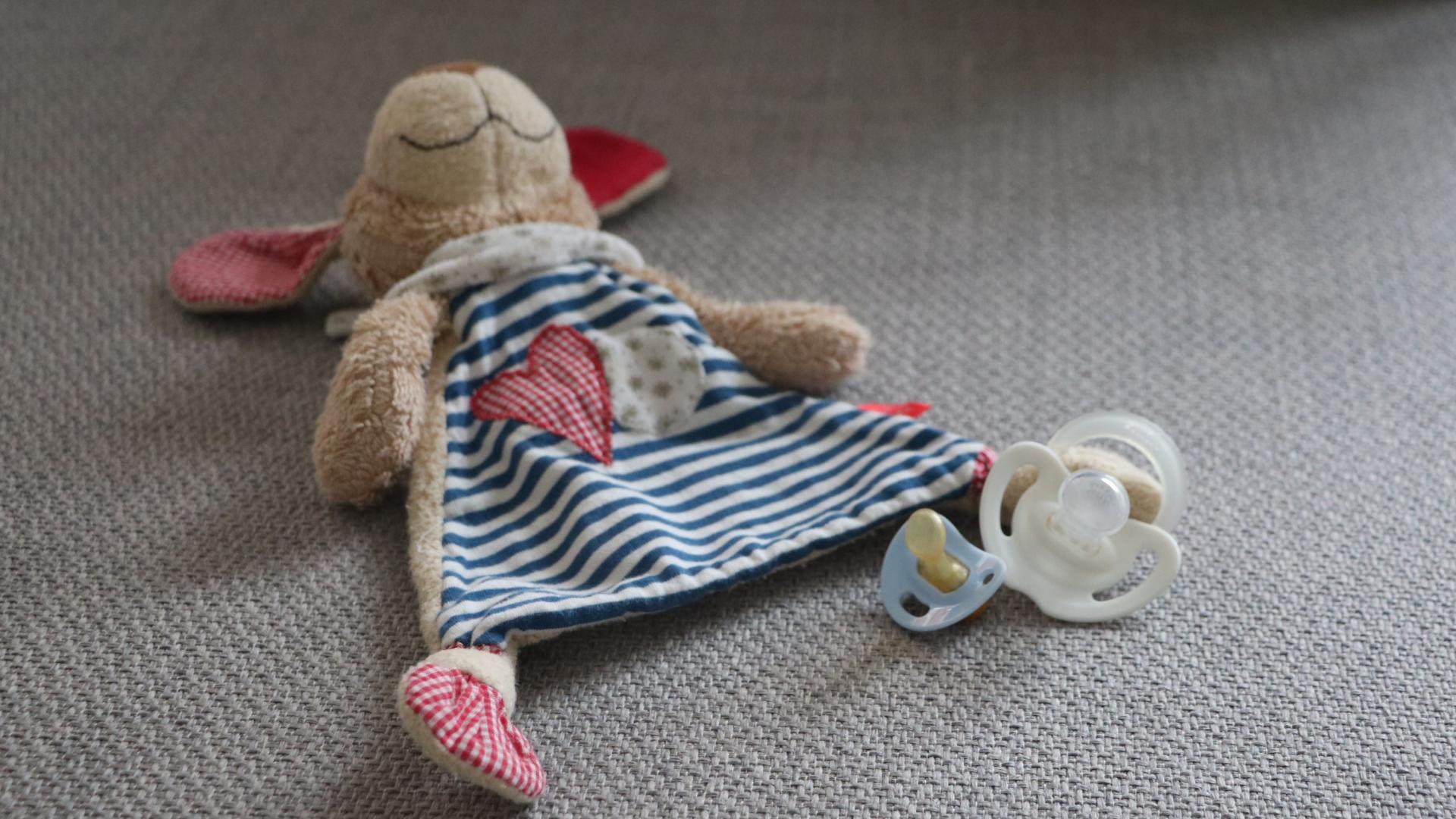 Neben einem Kuscheltier liegen ein kleiner und ein großer Schnuller