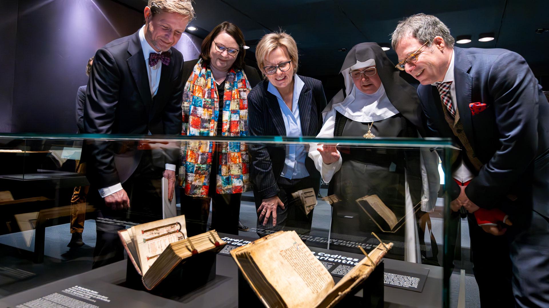 Vier Personen betrachten Bücher in einer Vitrine