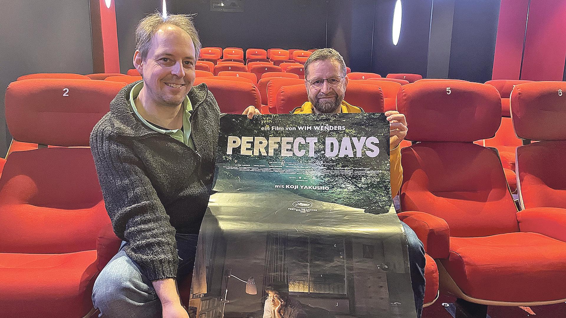 Zwei Männer im Kino halten ein Plakat.
