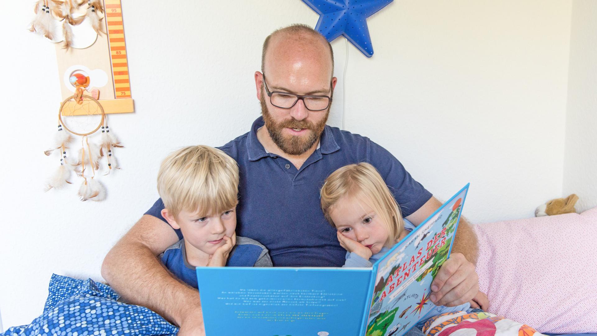 Ein Vater liest mit seinen zwei Kindern in einem Buch