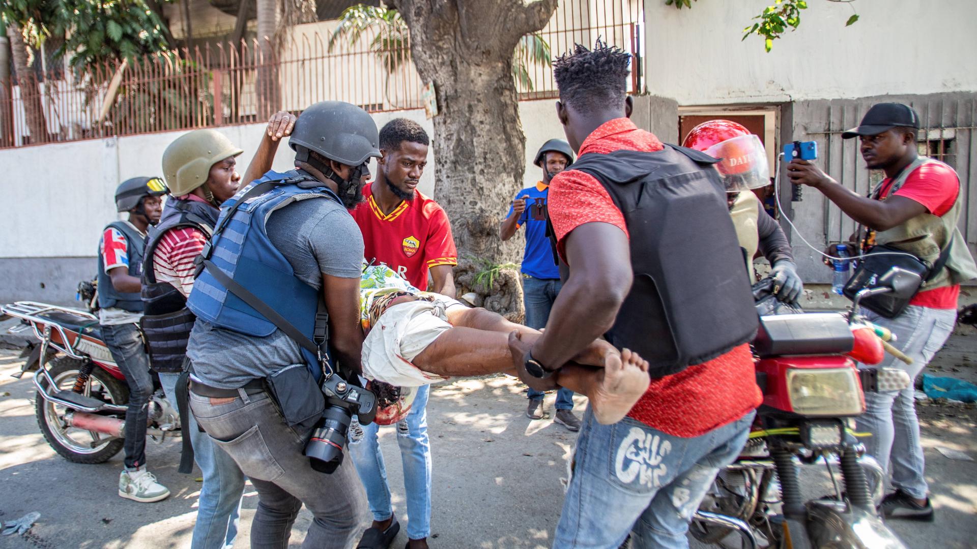 Vier Männer mit Schutzwesten und Helmen tragen eine verletzte Frau