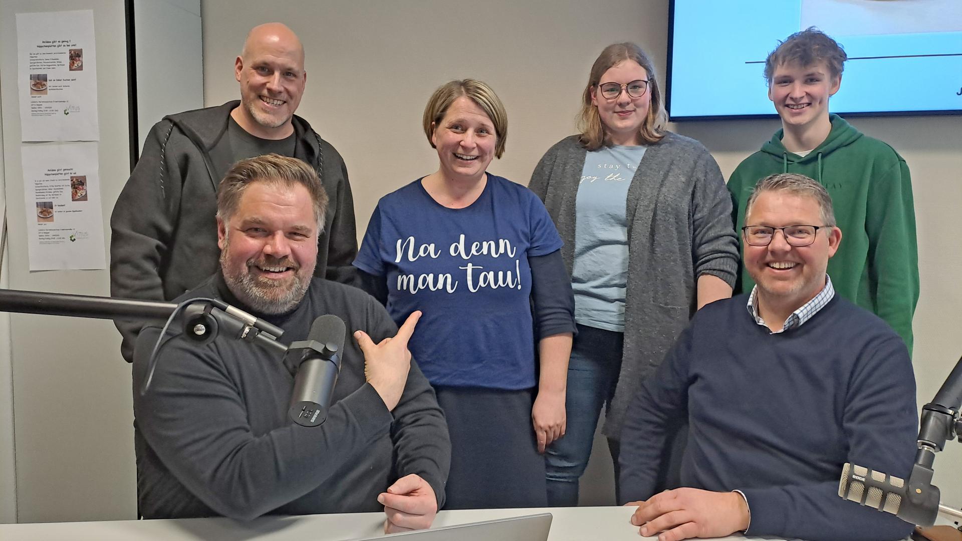 Sechs Menschen sitzen vor einem Mikrofon in einem Hörfunkstudio