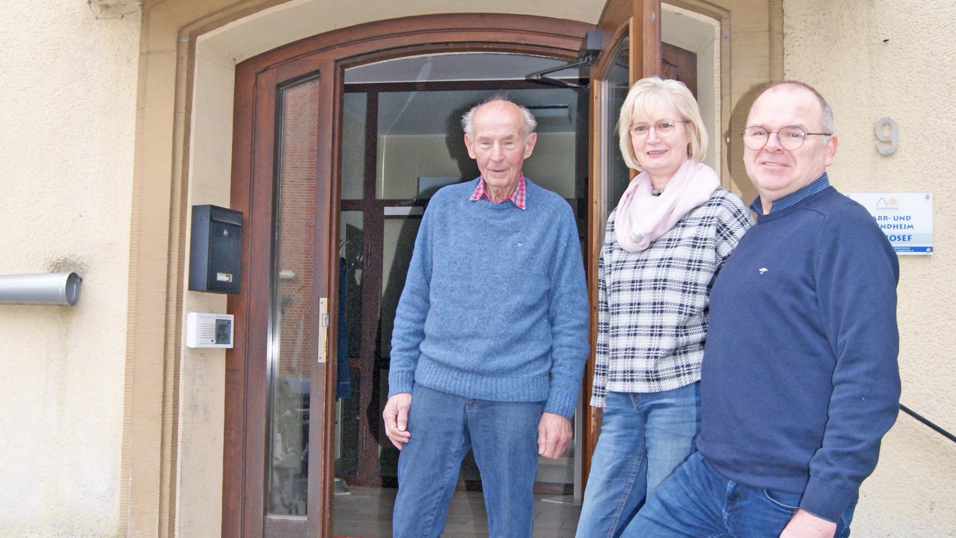 Zwei Männer und eine Frau stehen vor einer offenen Eingangstür. Oben der Schriftzug Sankt Josefsheim