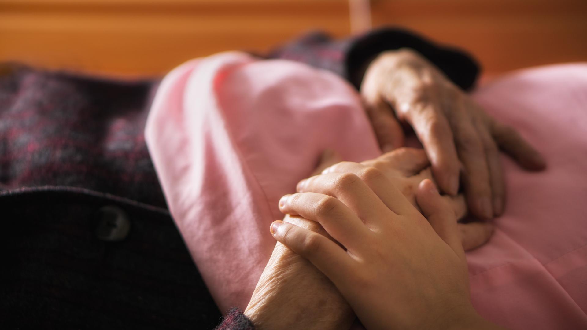 Zu sehen sind zwei Paar Hände auf einer Bettdecke , die sich umfassen.