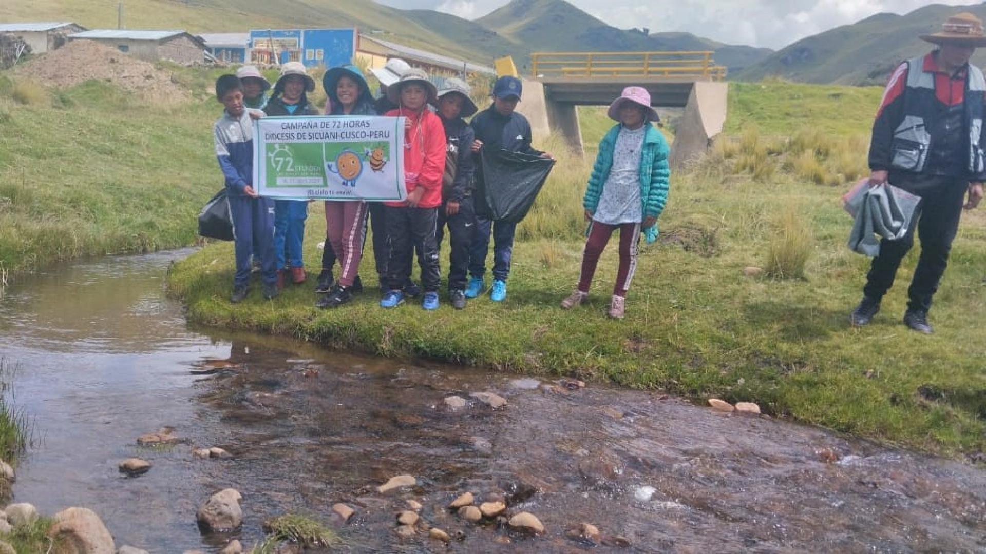 Eine Gruppe junger Südamerikaner steht auf einer Wiese vor einem Bach und hält ein Plakat
