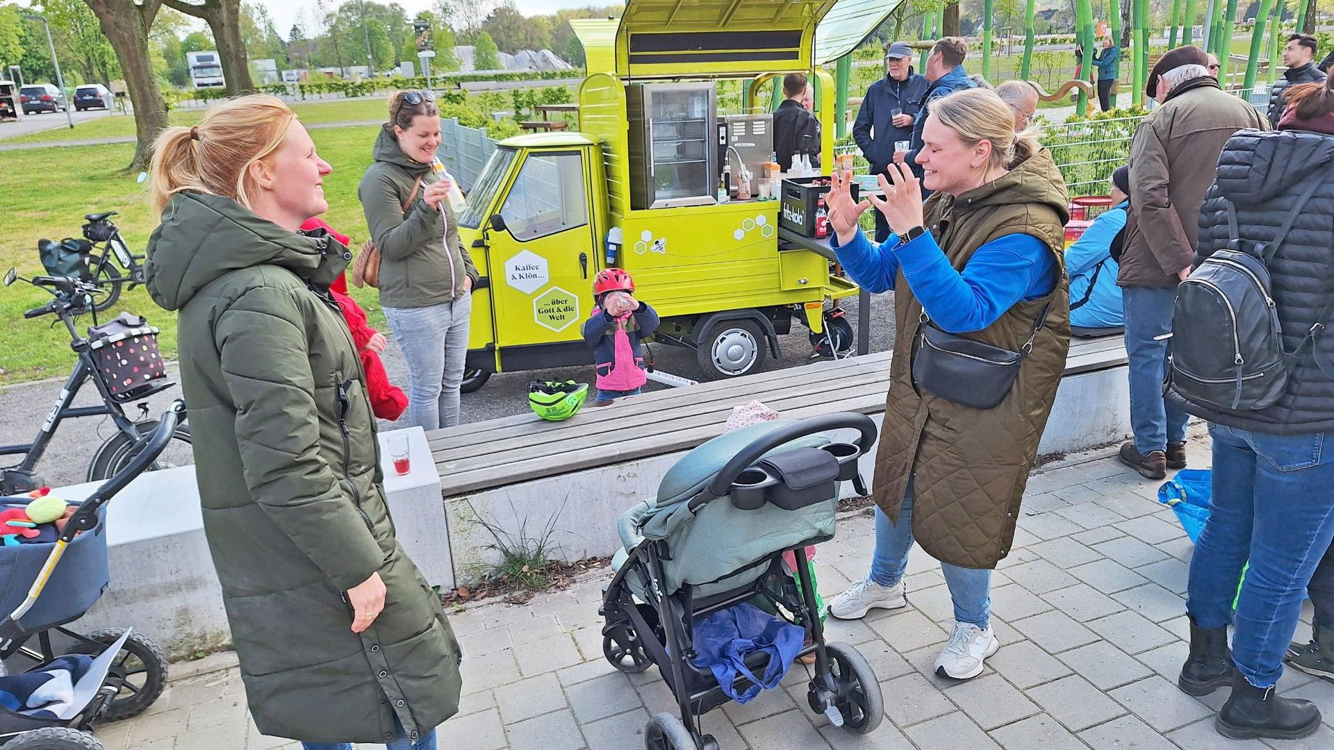 Zwei Frauen mit Kinderwagen unterhalten sich. Im Hintergrund ein Kleintransporter