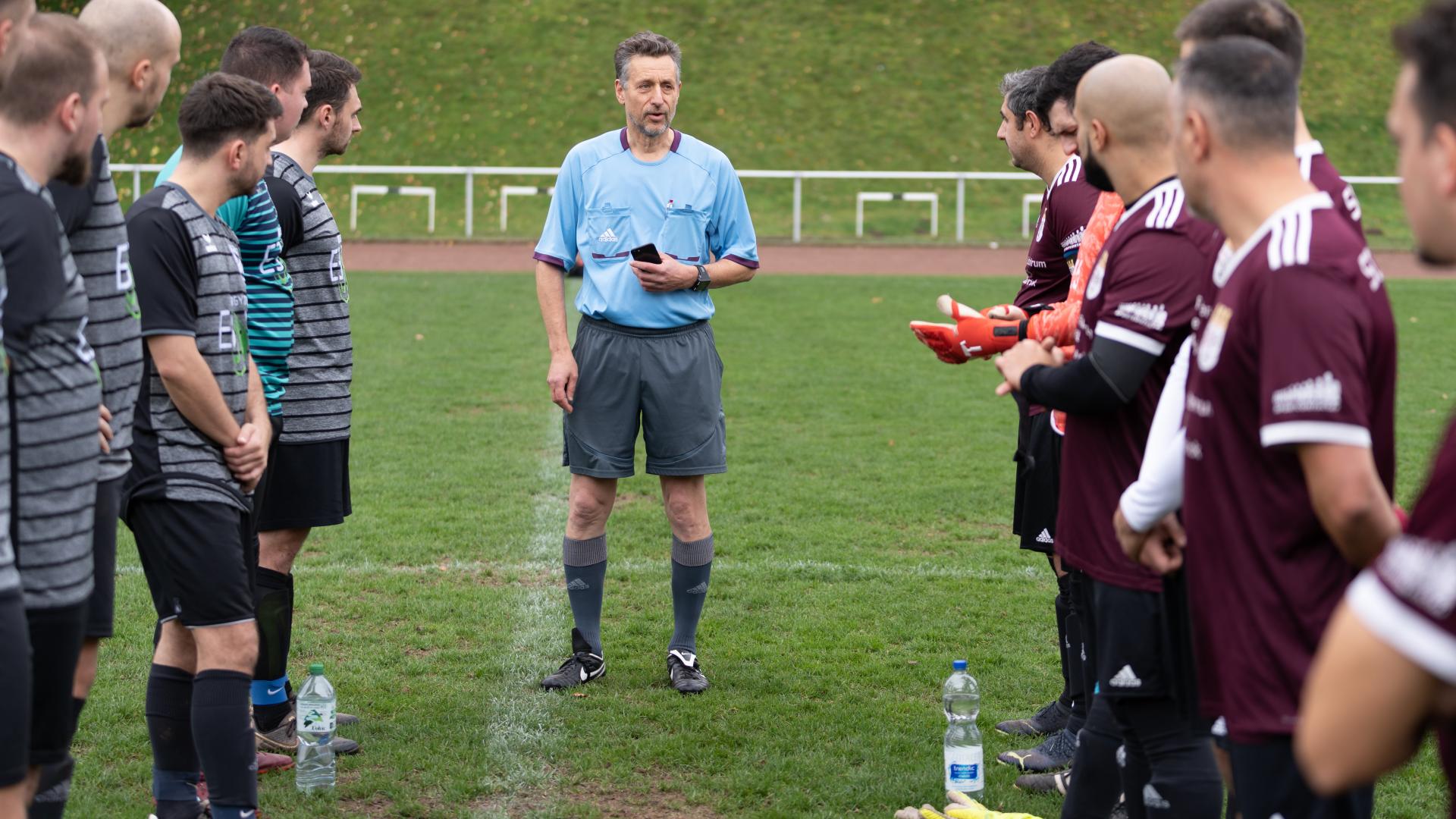 Ein Fußballschiedsrichter steht auf dem Spielfeld zwischen zwei Mannschaften