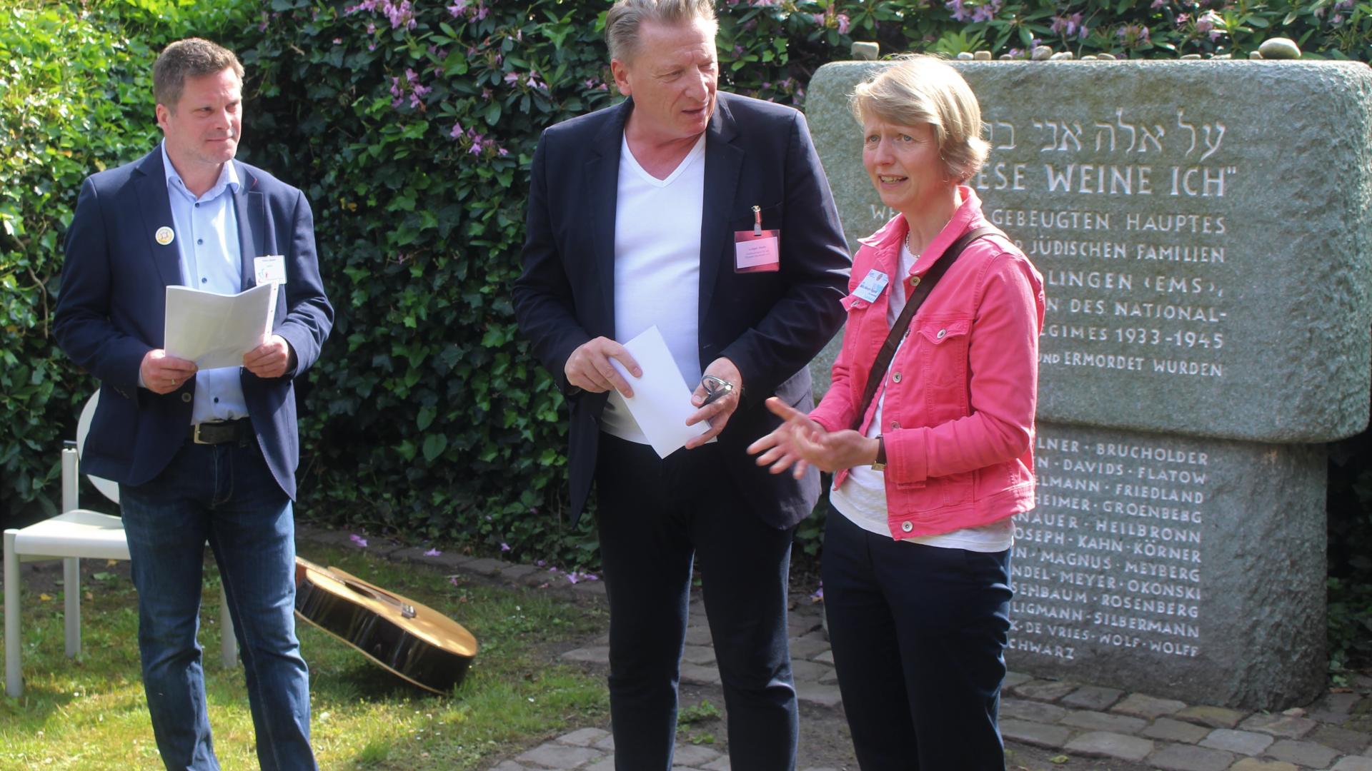 Drei Personen stehen vor einem Gedenkstein